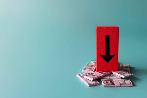 Salary reduction, recession, financial crisis. Red wooden cube with downward arrow and banknotes.